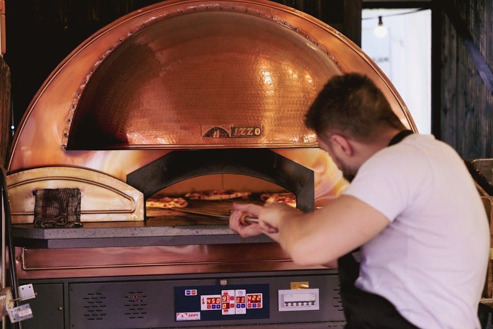 Pizza being prepared near a traditional oven